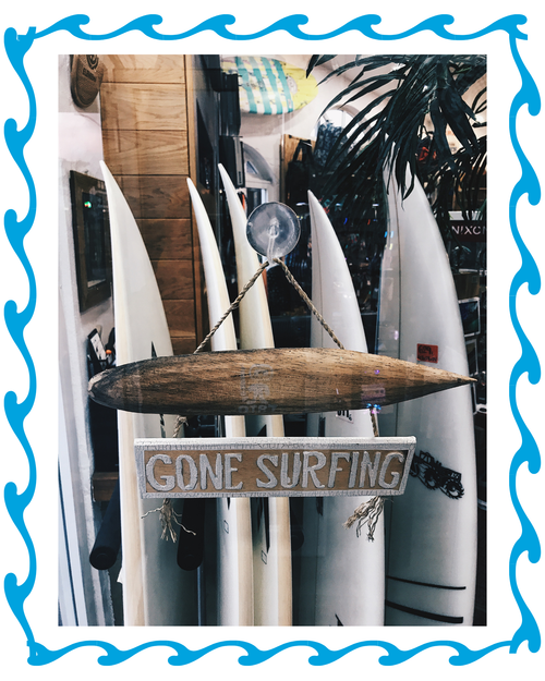 Gone Surfing rustic wooden surfboard sign with blue wave border frame and surfboards in background